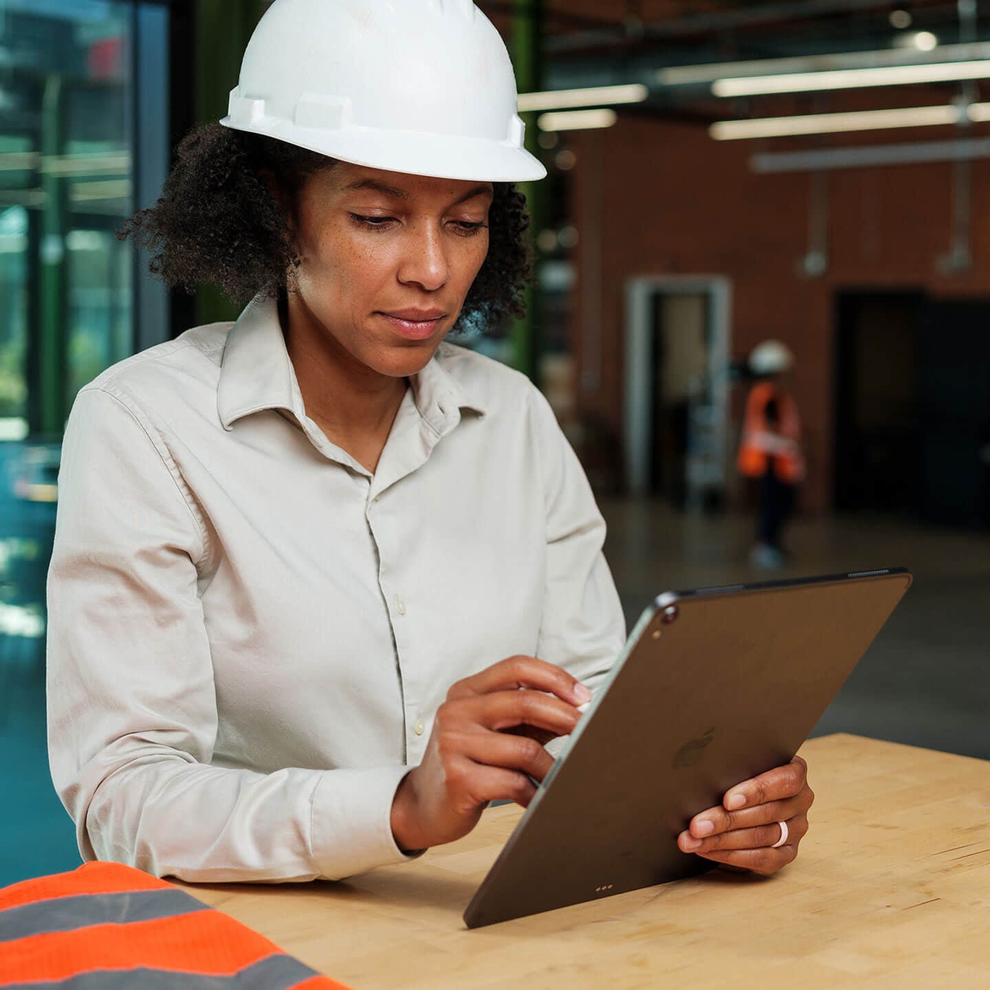 person standing at desk with hard hat using a tablet